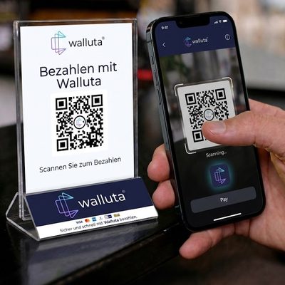 Thekenaufsteller „Bezahlen mit Walluta“ mit QR-Code, daneben scannt eine Hand den Code mit dem Smartphone